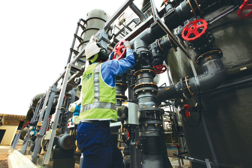 Man in safety vest turning wheel on pipework.
