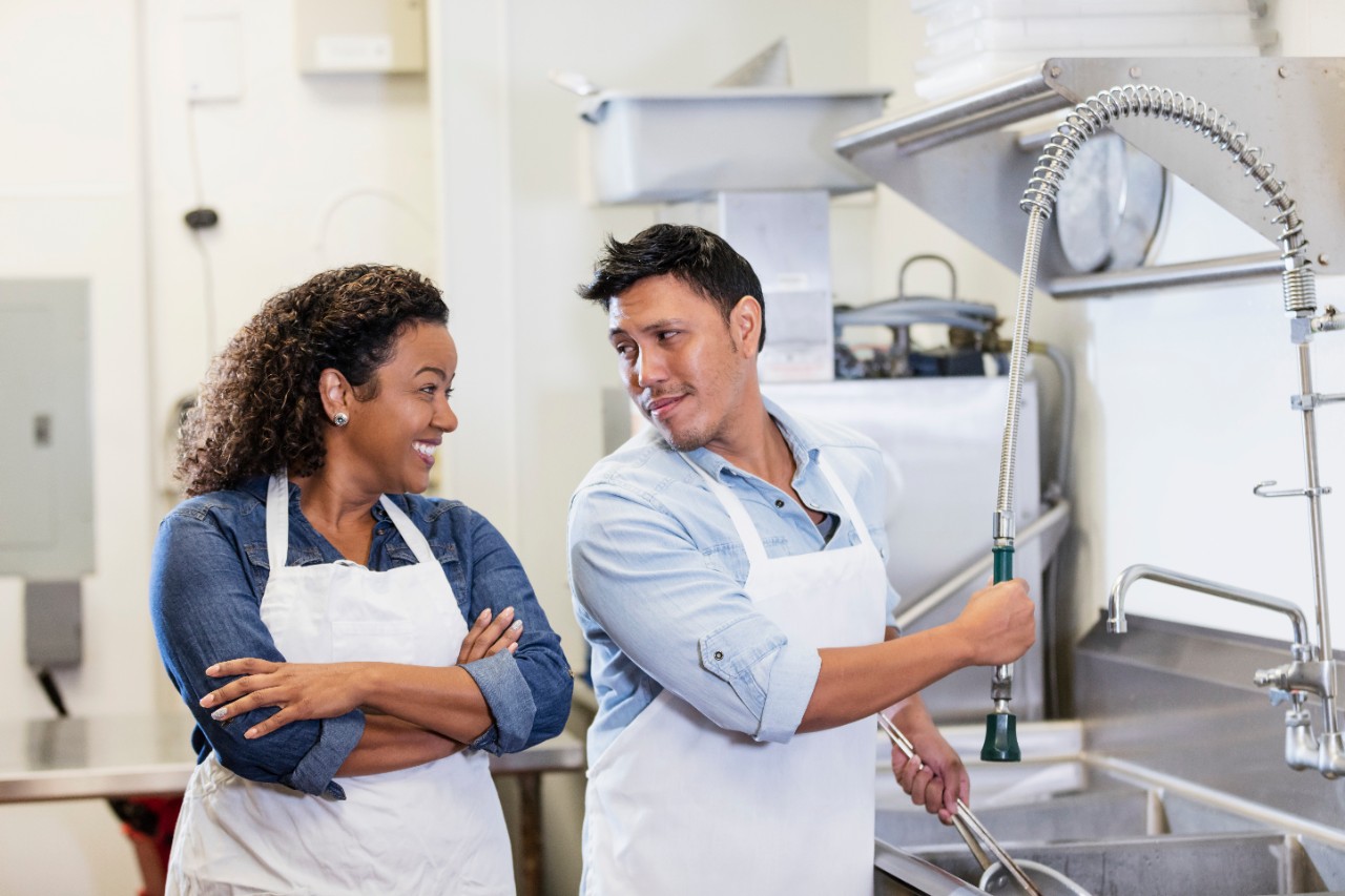 Couple washing dishes in commercial kitchen using spray rinse valve